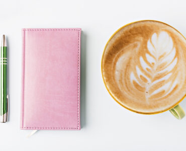 closed notebook with pen and coffee, flat lay