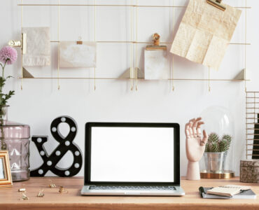 Laptop with mock-up screen, golden frame notes organizer and creative decorations on a wooden desk in a hipster work space interior