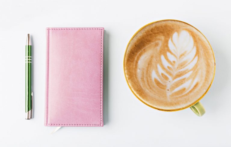 closed notebook with pen and coffee, flat lay